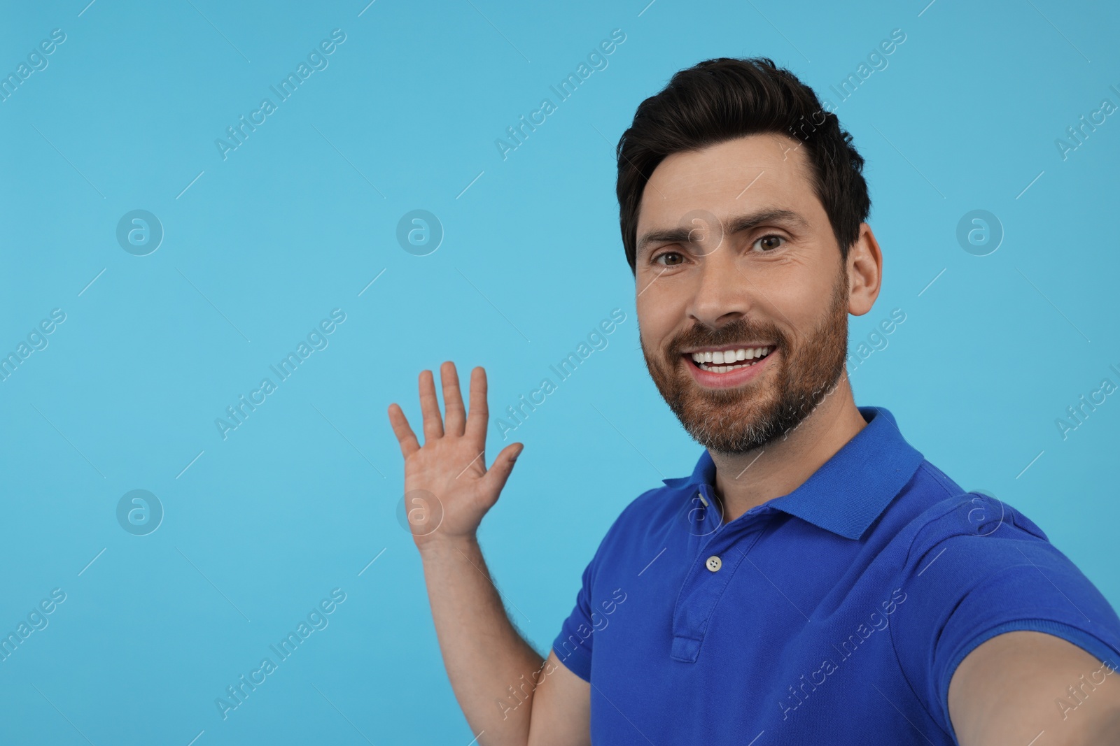 Photo of Smiling man taking selfie on light blue background, space for text