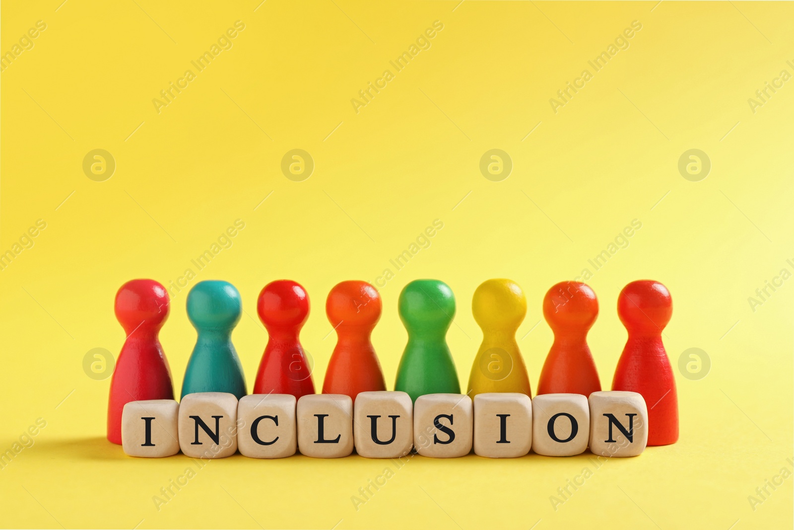 Photo of Colorful pawns and wooden cubes with word Inclusion on yellow background