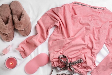 Photo of Flat lay composition with fluffy slippers and pajamas on white bedsheet. Comfortable home outfit