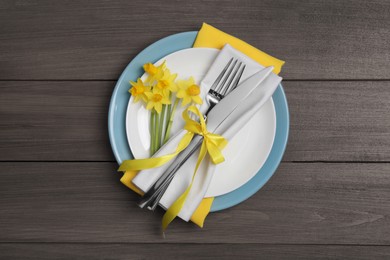 Festive table setting with narcissuses and cutlery on wooden background, top view. Easter celebration