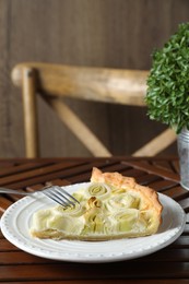 Plate with piece of tasty leek pie and fork on wooden table