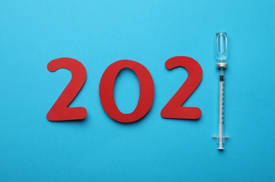 Photo of Paper numbers, syringe and vial with coronavirus vaccine forming 2021 on light blue background, flat lay