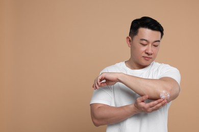 Photo of Handsome man applying body cream onto his elbow on light brown background. Space for text