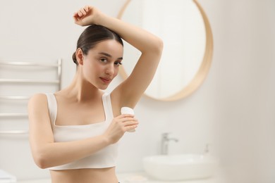 Beautiful woman applying deodorant in bathroom, space for text
