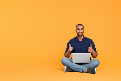 Smiling young man with laptop showing thumbs up on yellow background, space for text