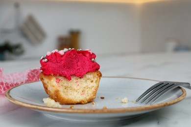Photo of Bitten cupcake with cream on plate, closeup
