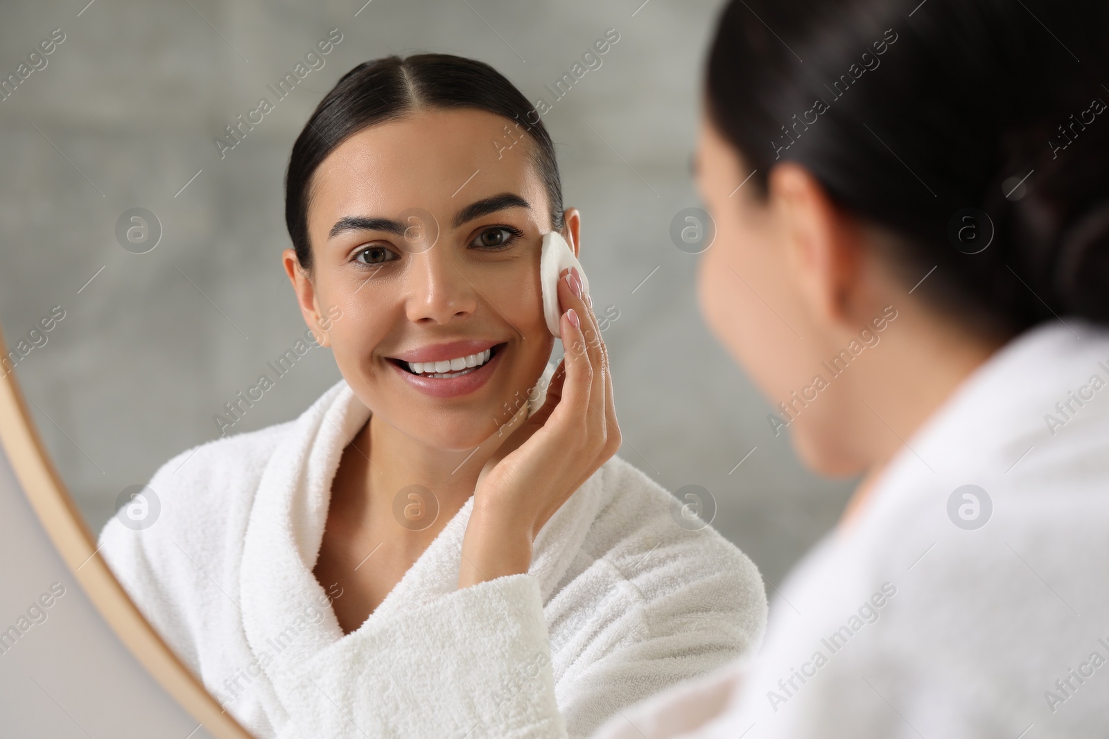 Photo of Beautiful woman removing makeup with cotton pad near mirror indoors