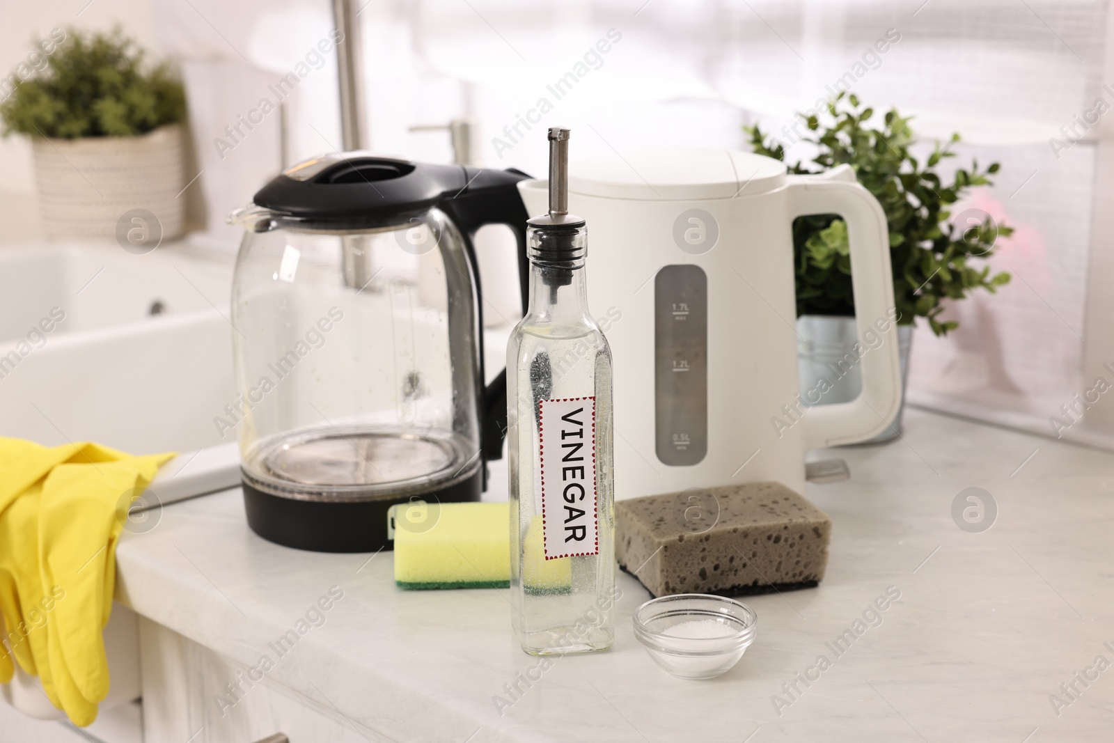 Photo of Cleaning electric kettle. Bottle of vinegar, sponges and baking soda on countertop in kitchen