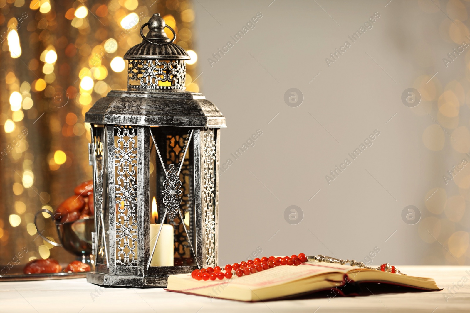 Photo of Arabic lantern, Quran, misbaha and dates on table against blurred lights, space for text