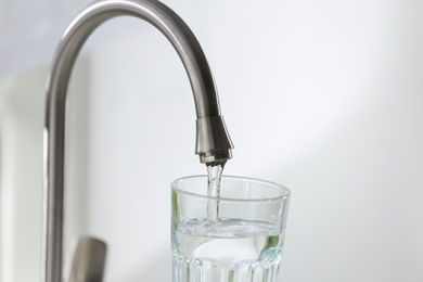 Photo of Filling glass with clear water from faucet on light background, closeup