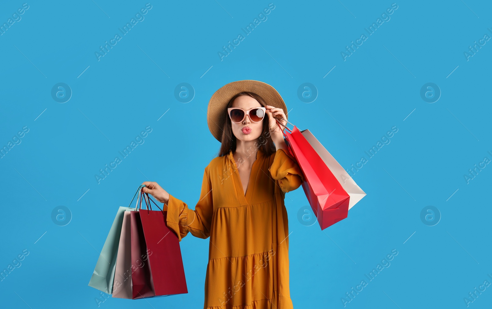 Photo of Beautiful young woman with paper shopping bags on light blue background