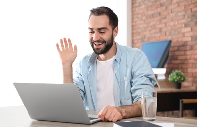 Young man using video chat on laptop in home office