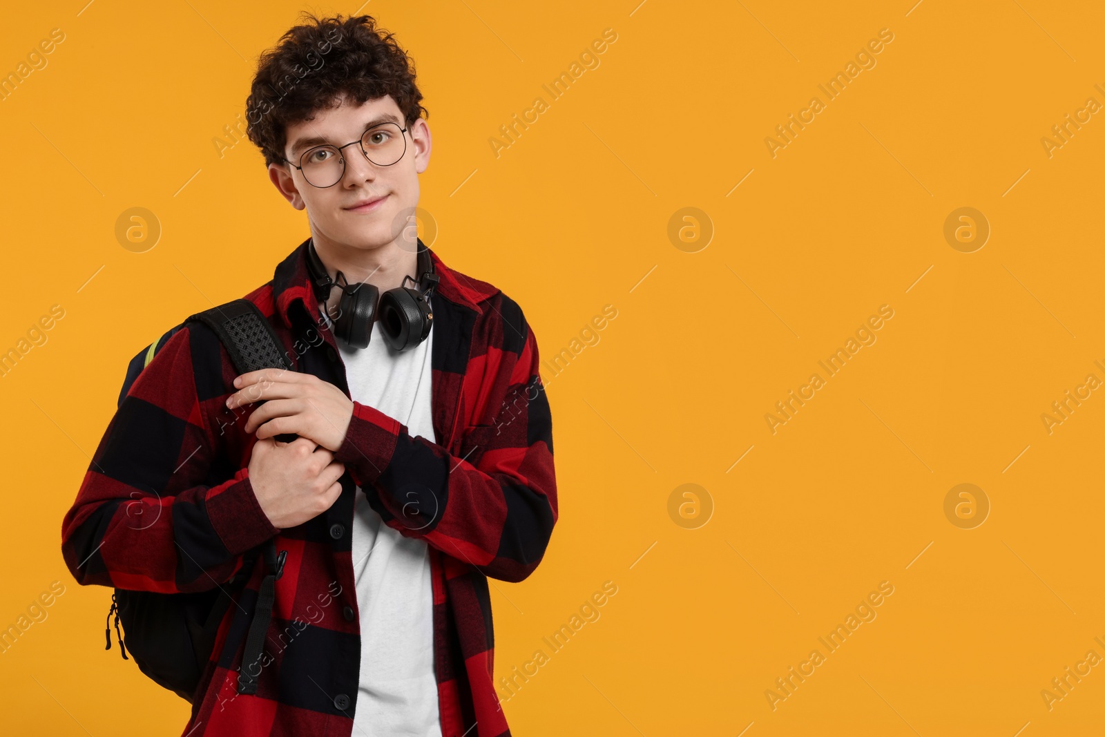 Photo of Portrait of student with backpack, headphones and glasses on orange background. Space for text