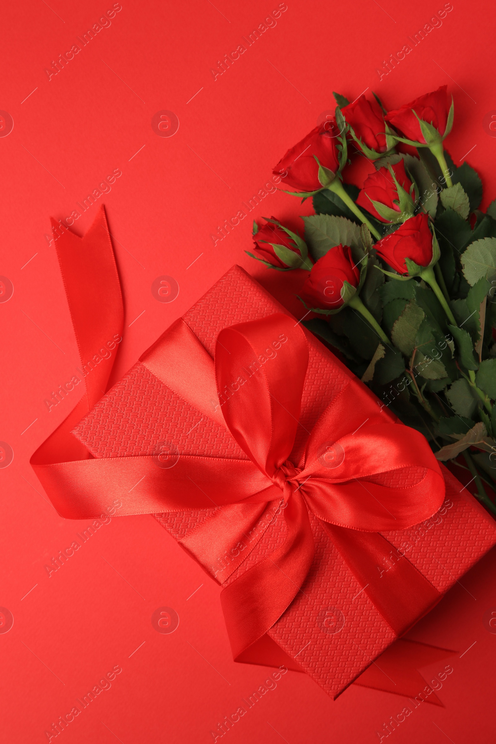 Photo of Beautiful gift box with bow and roses on red background, flat lay