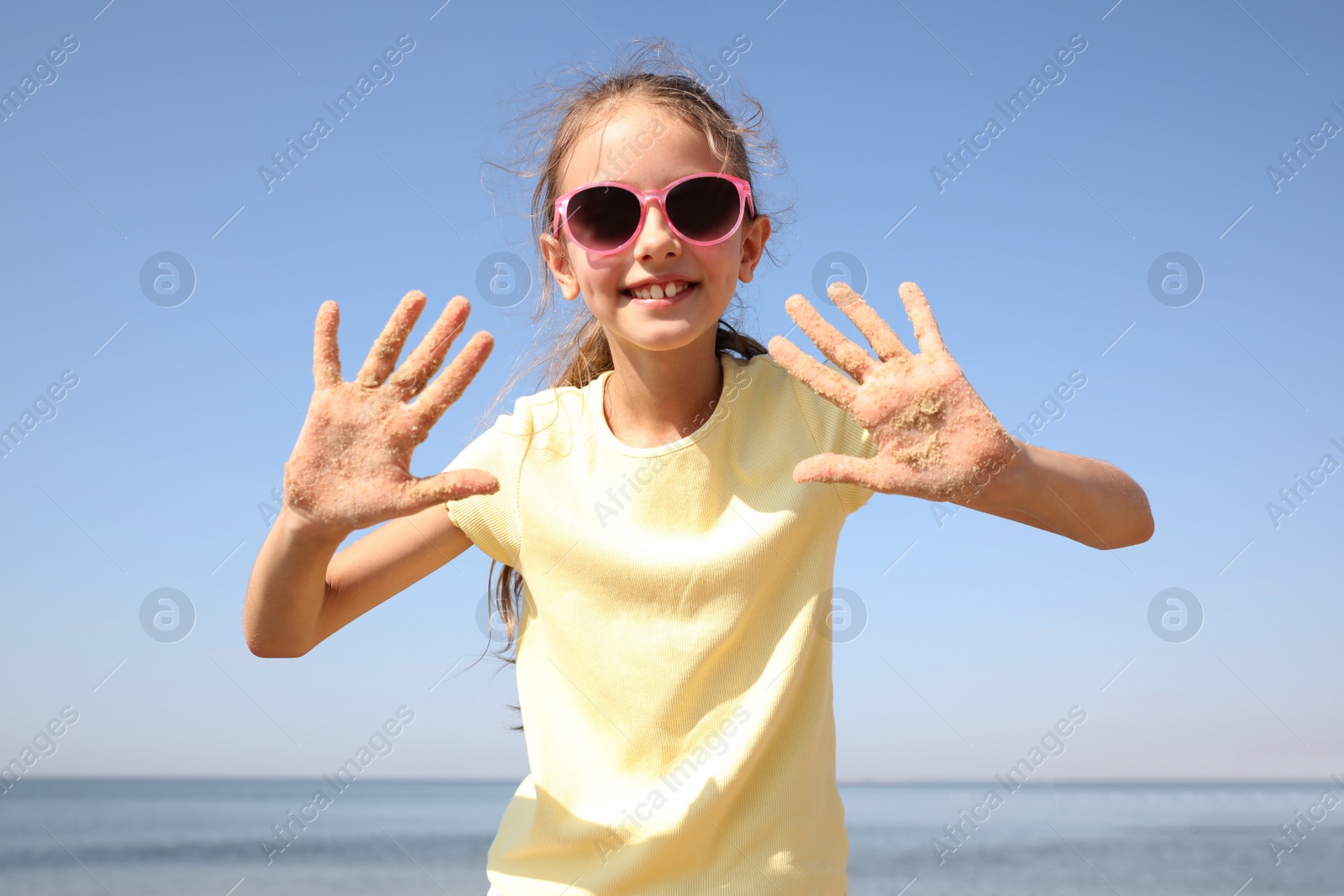 Photo of Cute girl showing hands covered with sand at beach