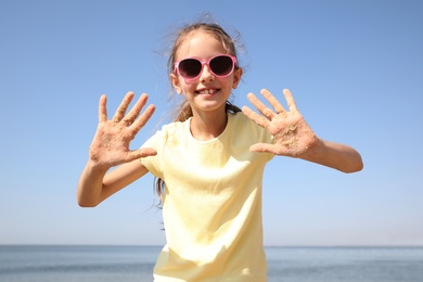 Photo of Cute girl showing hands covered with sand at beach