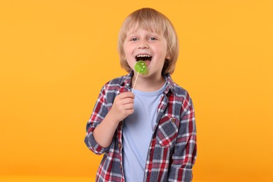 Happy little boy licking lollipop on orange background