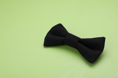 Photo of Stylish black bow tie on light green background. Space for text