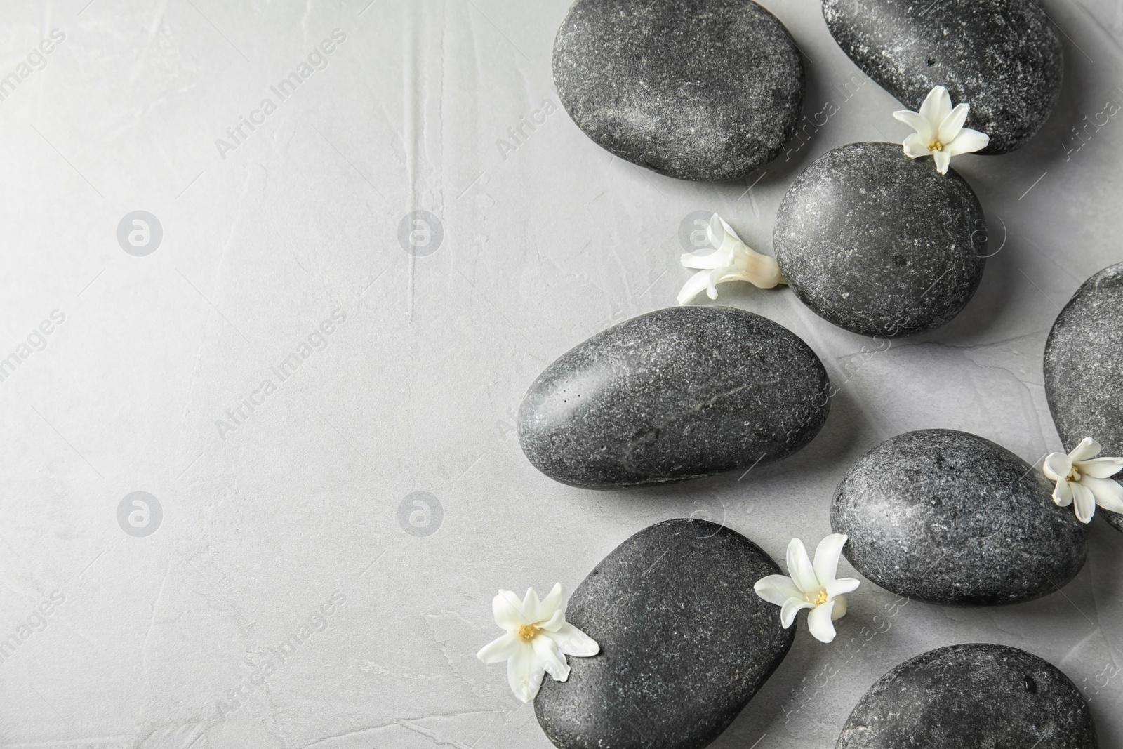 Photo of Zen stones and exotic flowers on grey background, top view with space for text