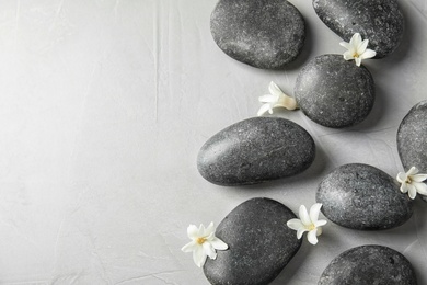 Zen stones and exotic flowers on grey background, top view with space for text