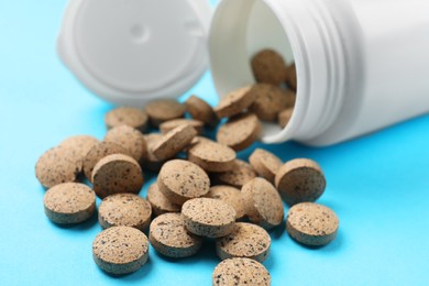 Photo of Bottle and vitamin pills on light blue background, closeup