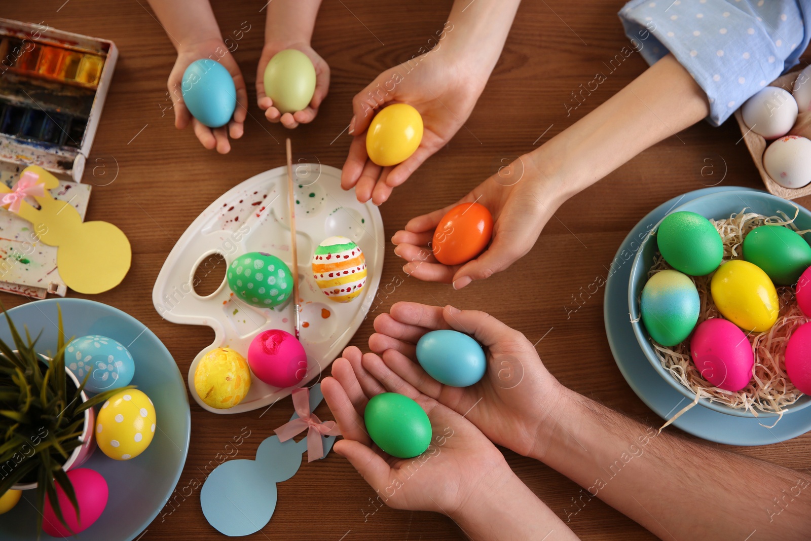 Photo of Father, mother and their child painting Easter eggs at wooden table, top view