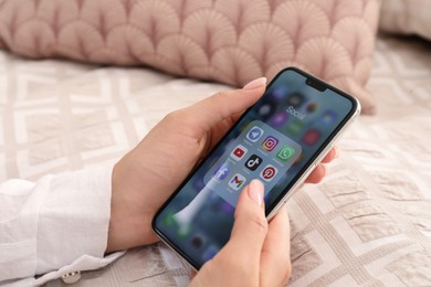 Photo of MYKOLAIV, UKRAINE - AUGUST 11, 2021: Woman using Apple iPhone X at bed, closeup. Screen with different social media icons