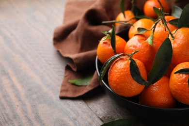 Photo of Fresh ripe tangerines with green leaves on wooden table, closeup. Space for text