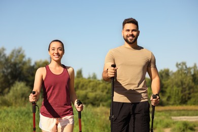 Happy couple practicing Nordic walking with poles outdoors on sunny day