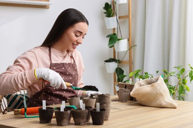 Young woman adding soil into peat pots at wooden table indoors. Growing vegetable seeds