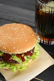 Photo of Burger with delicious patty and soda drink on black wooden table
