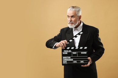 Photo of Senior actor holding clapperboard on beige background, space for text. Film industry