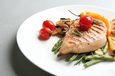 Tasty grilled chicken fillet with vegetables on light grey table, closeup