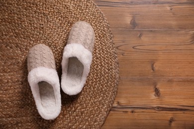 Pair of warm stylish slippers and wicker mat on wooden floor, flat lay. Space for text