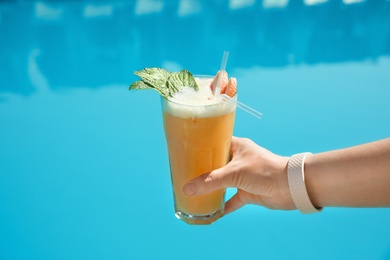 Photo of Woman with refreshing cocktail near swimming pool outdoors, closeup