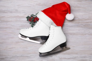 Photo of Pair of ice skates, Christmas hat and decorative branch on white wooden background, flat lay