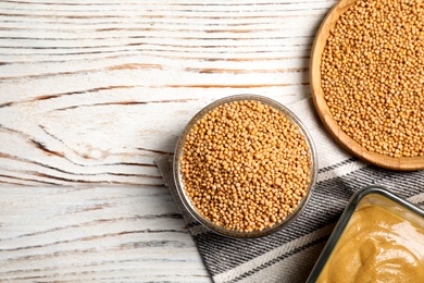 Flat lay composition with mustard seeds on white wooden table. Space for text