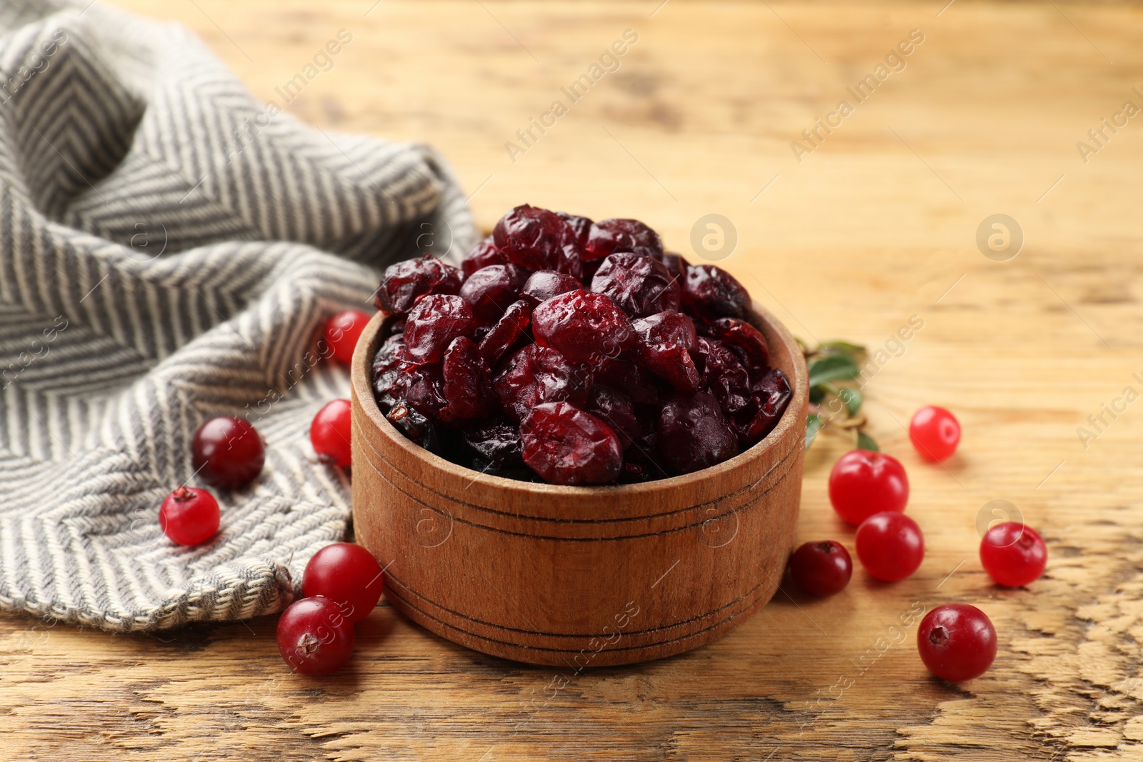 Photo of Tasty dried cranberries in bowl and fresh ones on wooden table, closeup