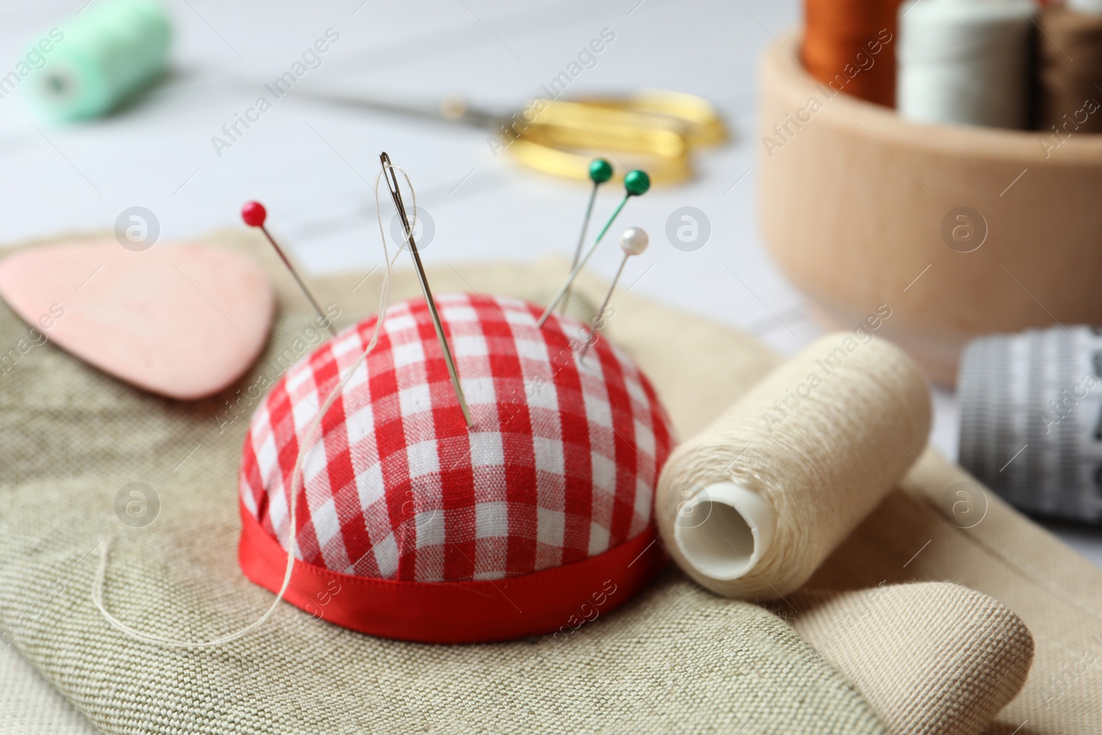 Photo of Pincushion, spools of threads and sewing tools on table, closeup