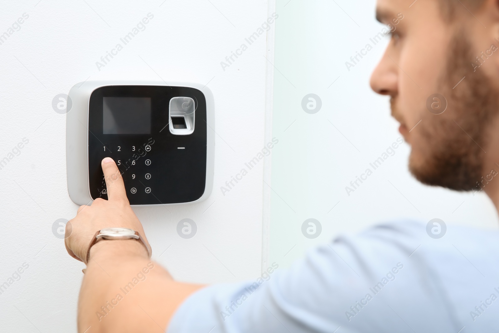 Photo of Young man entering code on alarm system keypad indoors