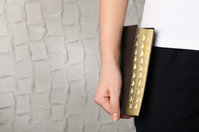 Photo of Woman holding Bible against white wall, closeup. Space for text