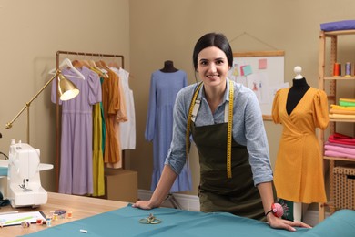 Photo of Dressmaker near table with light blue fabric in workshop