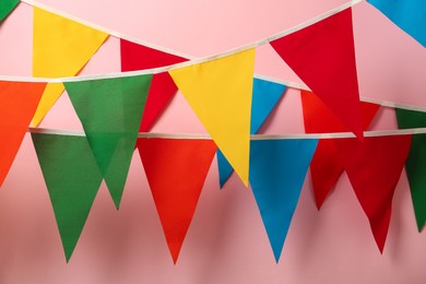 Photo of Buntings with colorful triangular flags hanging on pink background. Festive decor