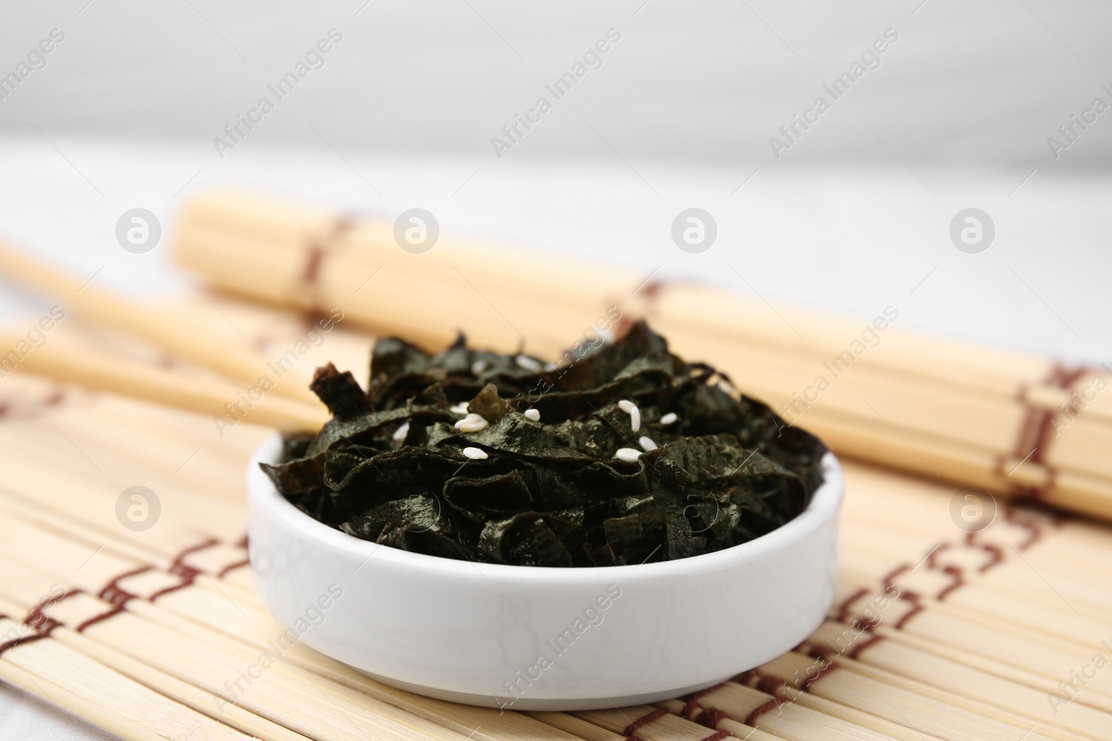 Photo of Chopped nori sheets with sesame and chopsticks on bamboo mat, closeup