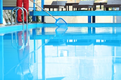 Photo of Male worker cleaning outdoor pool with scoop net