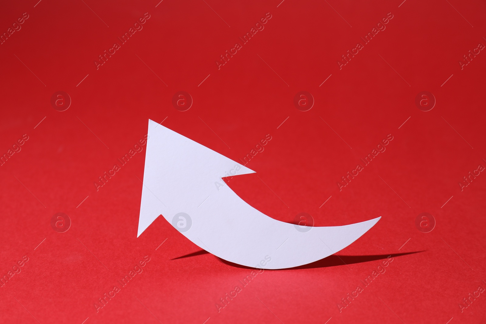 Photo of White curved paper arrow on red background