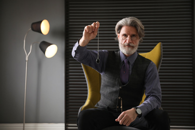 Photo of Psychotherapist with pendulum in office. Hypnotherapy session