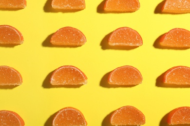 Photo of Delicious orange marmalade candies on yellow background, flat lay