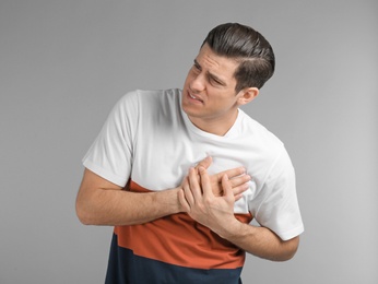 Young man suffering from chest pain on grey background