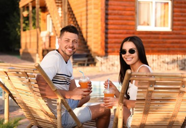 Image of Happy couple with cups of refreshing drink resting in deck chairs outdoors